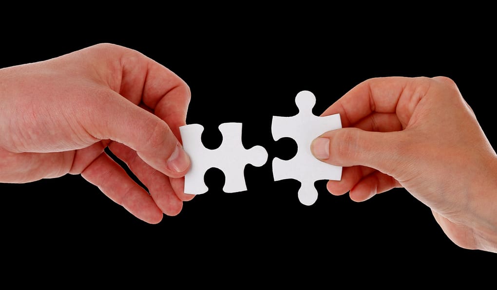 two hands holding up puzzle pieces that fit together, symbolizing collaborative decision making