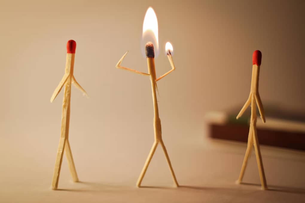 three matchsticks shaped like people. One of them is burning, signifying burnout due to poor work-life balance
