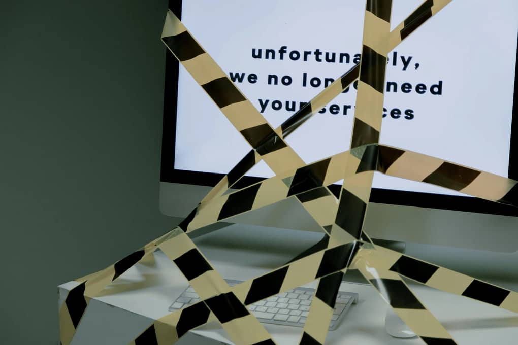 a computer monitor displaying the words "unfortunately, we no longer need your services". The monitor is also taped up by police tape. This image symbolizes what might happen during business restructuring