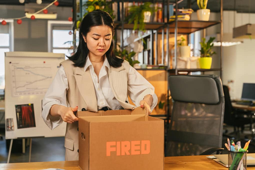 a young woman packing up her things from her office into a box labeled "fired". This is one of the many unfortunate scenarios when it comes to company restructuring
