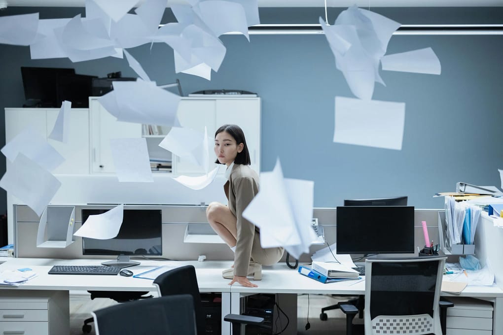an employee crouched on a desk with papers flying everywhere, symbolizing what happens without a good talent retention strategy