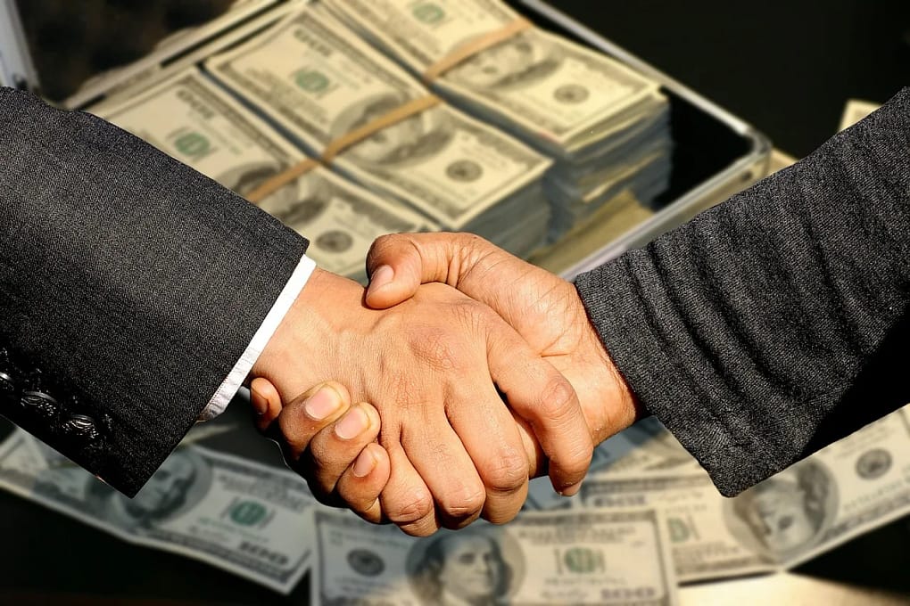 businessmen shaking hands in front of a background of piles of money, the ideal when it comes to business exit planning