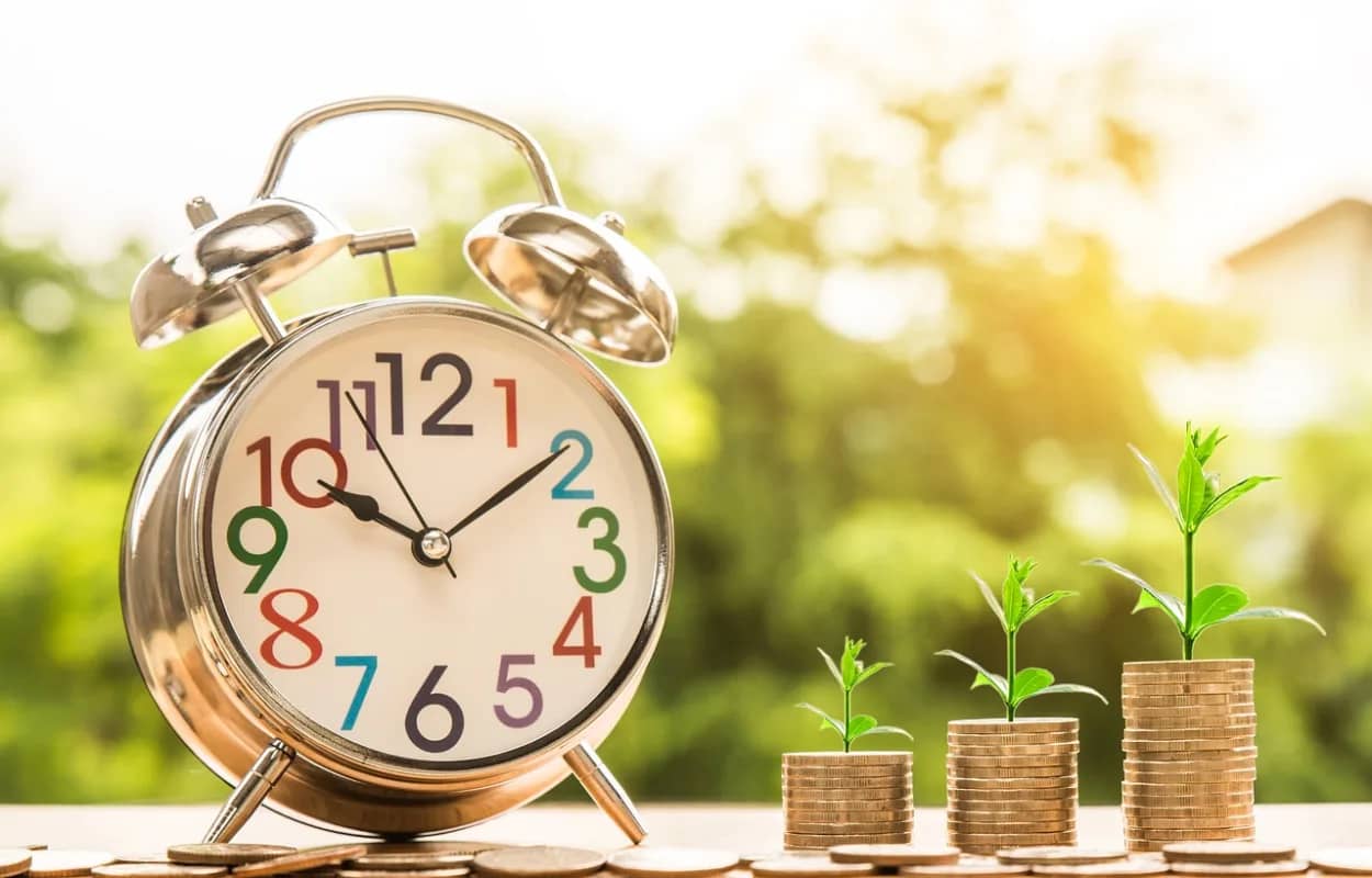 a clock with next to growing stacks of coins with plants growing on top of each stack, signifying cash flow and growth