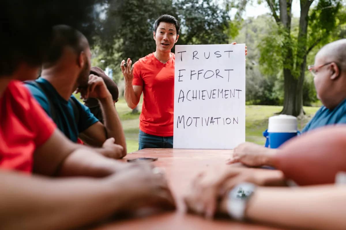 a team leader holding up a sign that says Trust, Effort, Achievement, and Motivation. The first letters of each word spell out "TEAM"
